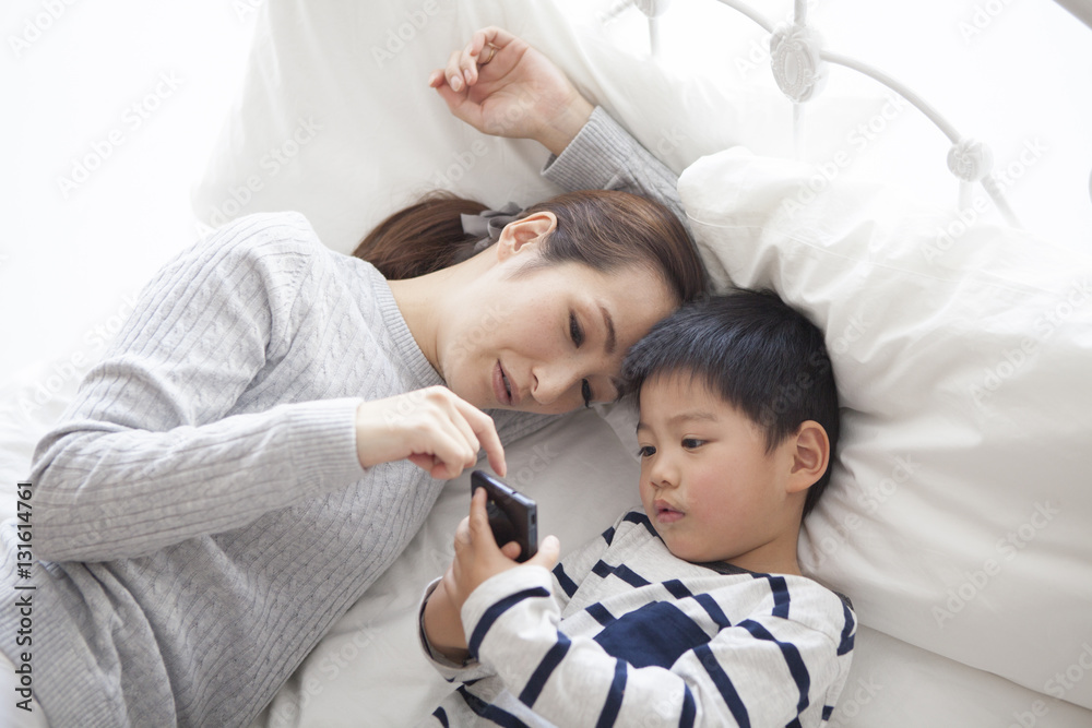 Mother and child are watching smartphone while sleeping in bed