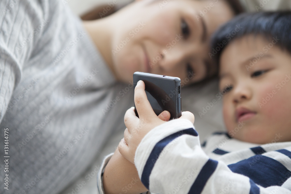 Mother and child are watching smartphone while sleeping in bed