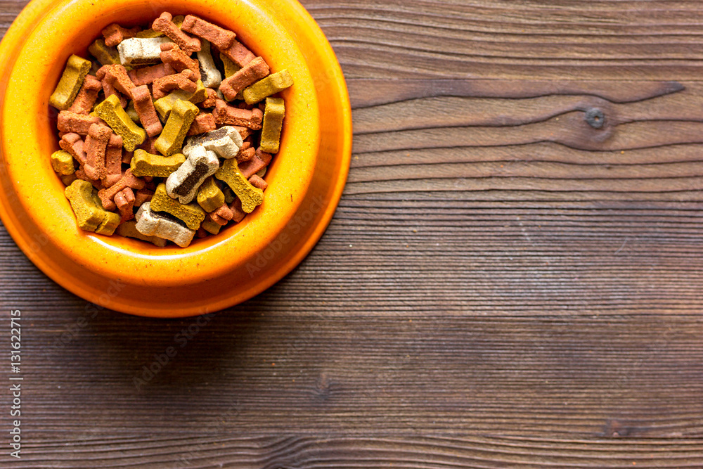 dry dog food in bowl on wooden background top view