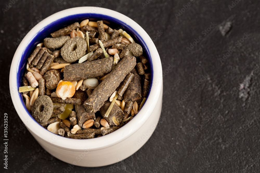 dry food for rodents in bowl dark background top view