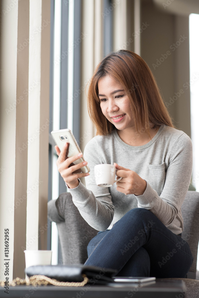 Woman using smartphone in coffee shop with image reflection on g