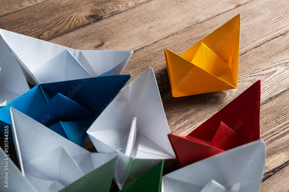 Business leadership concept with white and color paper boats on wooden table