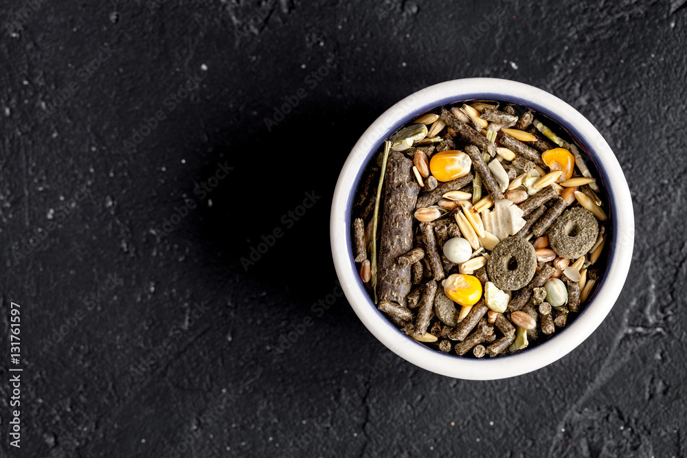 dry food for rodents in bowl dark background top view