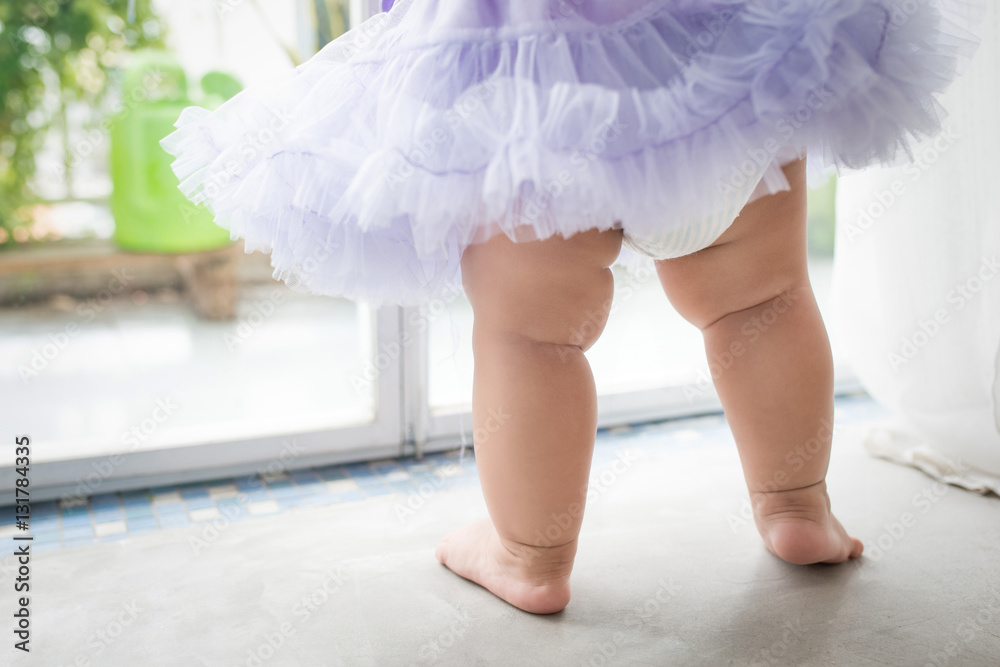 Little asian baby girl at home in white room stands near window.