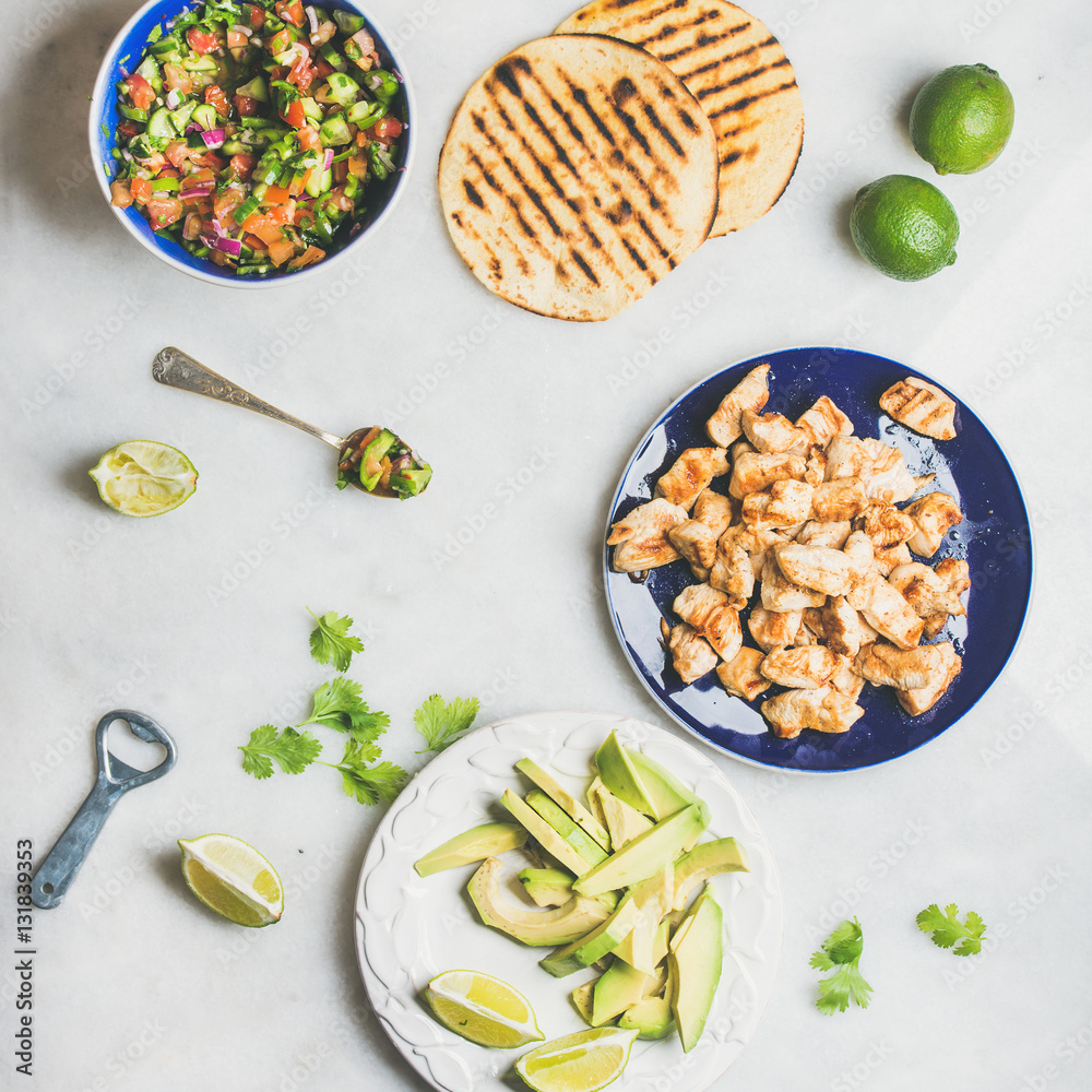 Ingredients for cooking chicken and avocado tacos. Fresh salsa, limes, grilled corn tortillas, grill