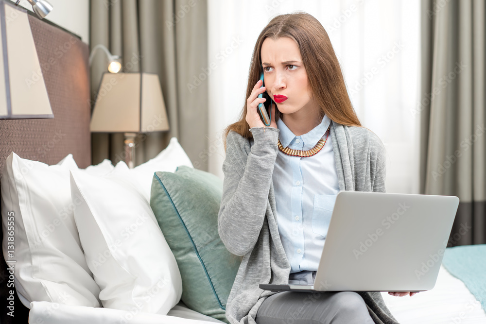 Displeased business woman calling with phone in the luxury hotel room. Staying at the hotel during t