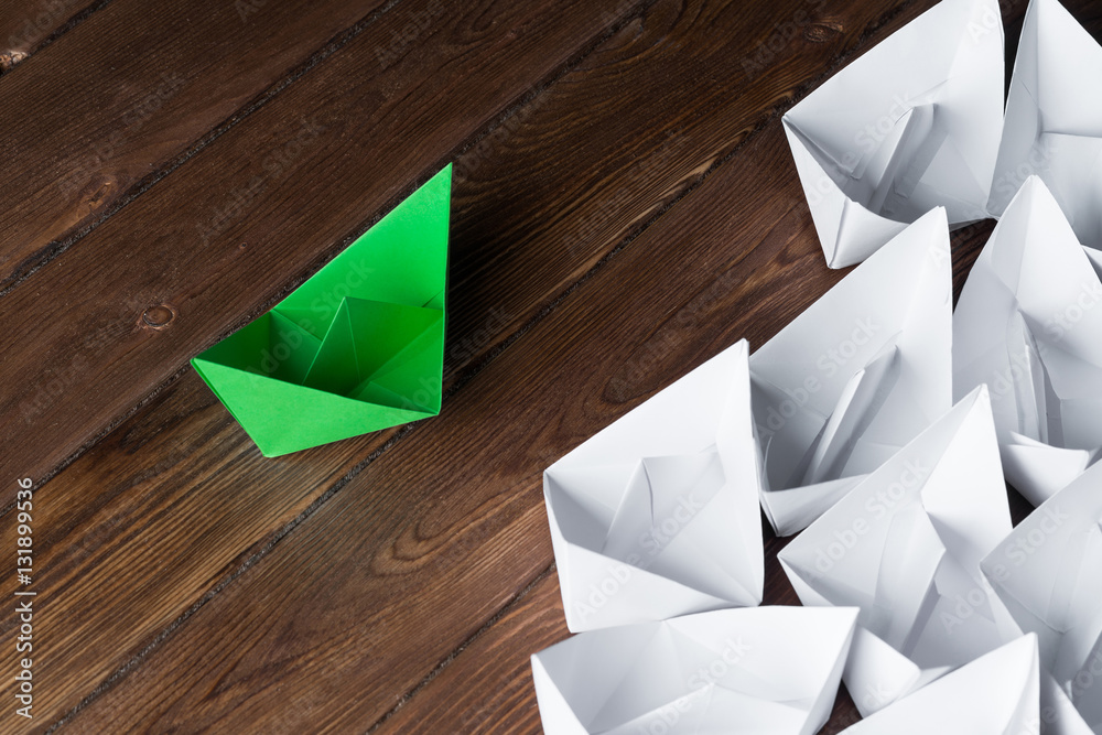 Business leadership concept with white and color paper boats on wooden table