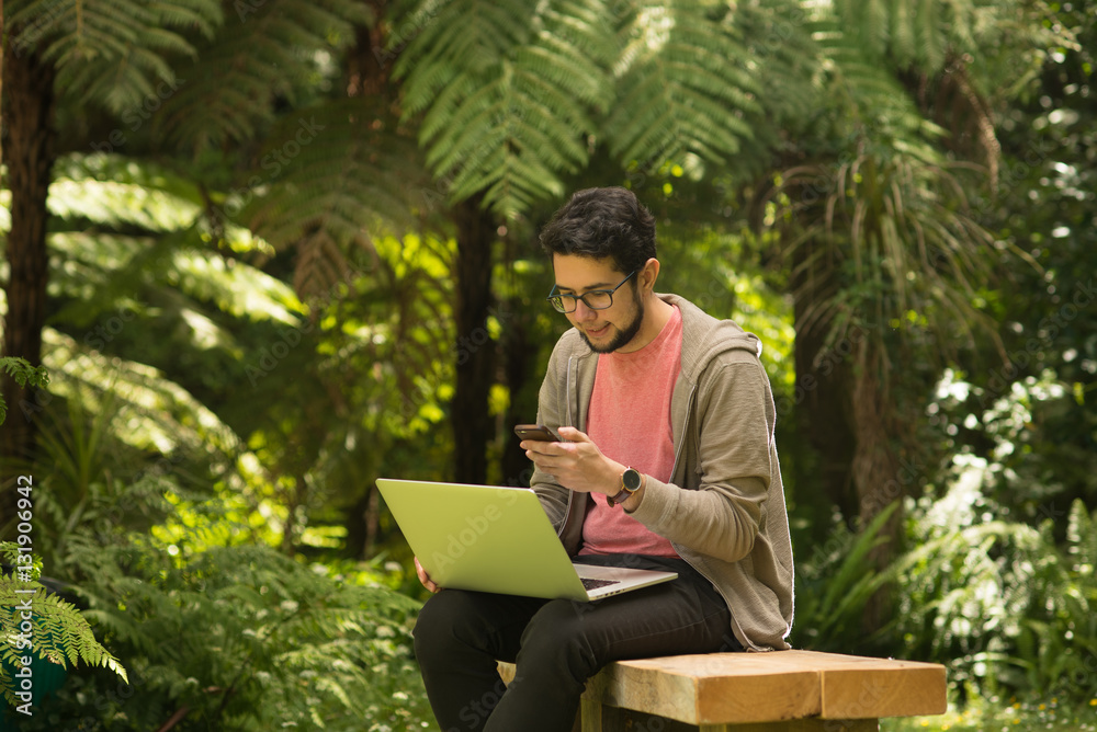 Young man with a laptop and smartphone sitting outdoor in a park