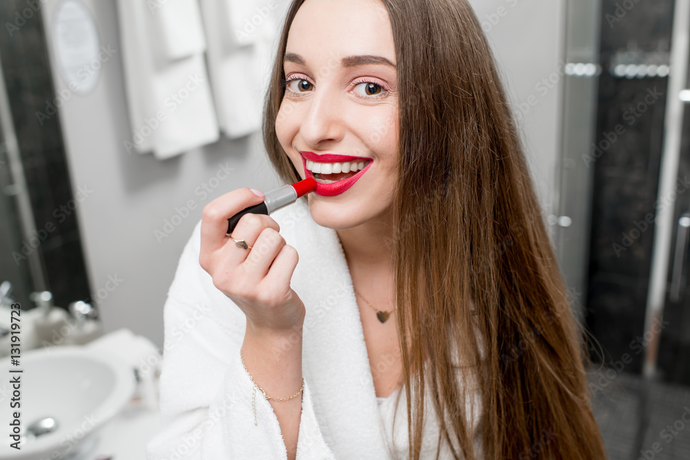 Young beautiful woman in bathrobe applying lipstick in the bathroom