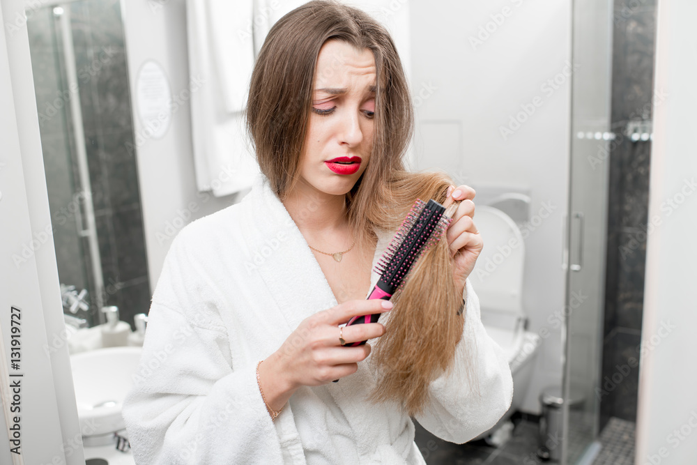 Woman worried about hairloss and splited hair ends standing with comb in the bathroom