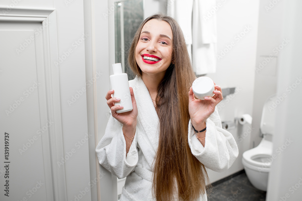 Happy woman holding bottles with lotion and cream in the bathroom