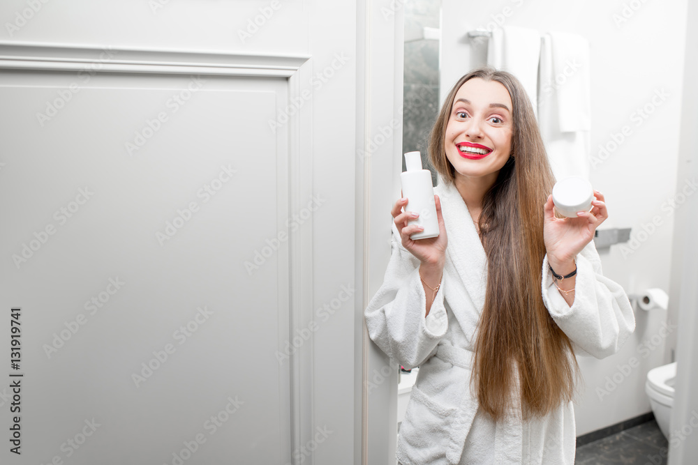 Happy woman holding bottles with lotion and cream in the bathroom