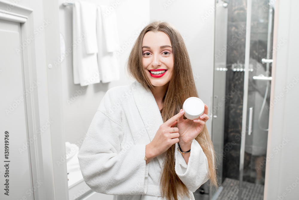 Happy woman holding bottle with cream in the bathroom