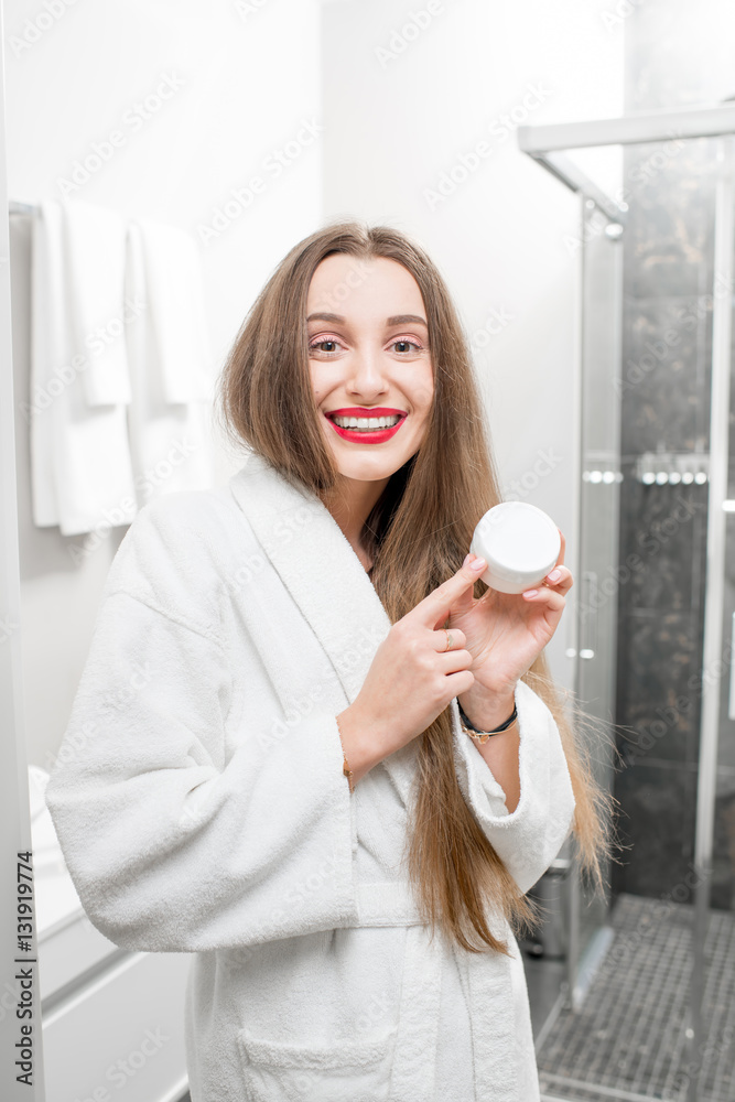 Happy woman holding bottle with cream in the bathroom