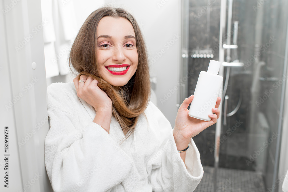 Happy woman with healthy hair holding a bottle with shampoo or conditioner in the bathroom