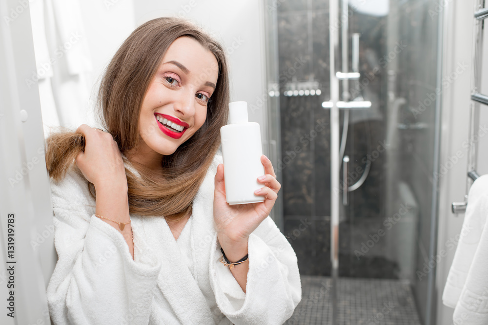 Happy woman with healthy hair holding a bottle with shampoo or conditioner in the bathroom