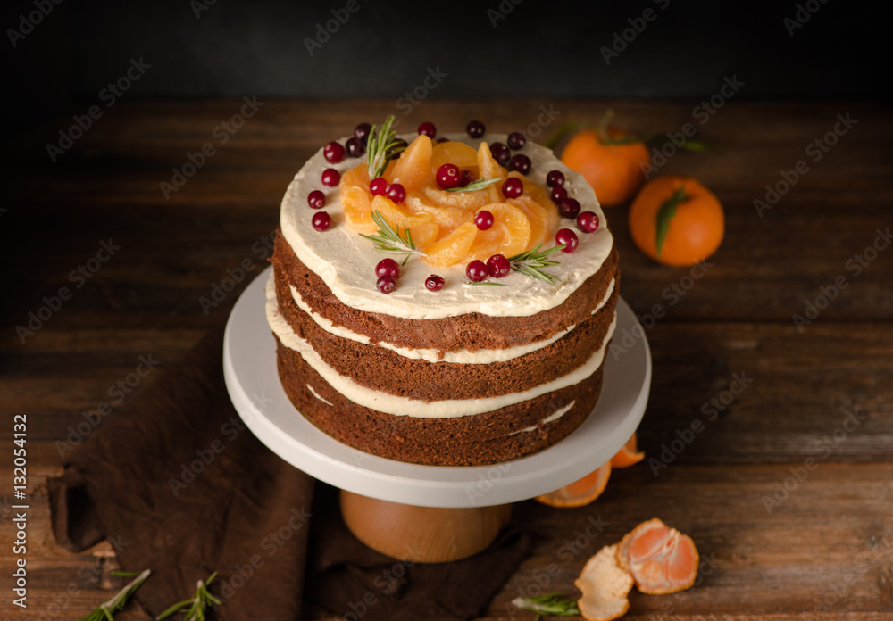 The chocolate cake with clementines, cranberry and rosemary on cakestand wooden background. Still li