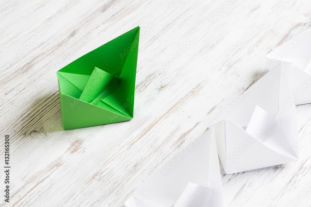 Business leadership concept with white and color paper boats on wooden table