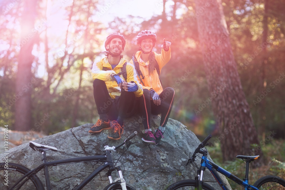 Biker couple sitting on rock and pointing in distance