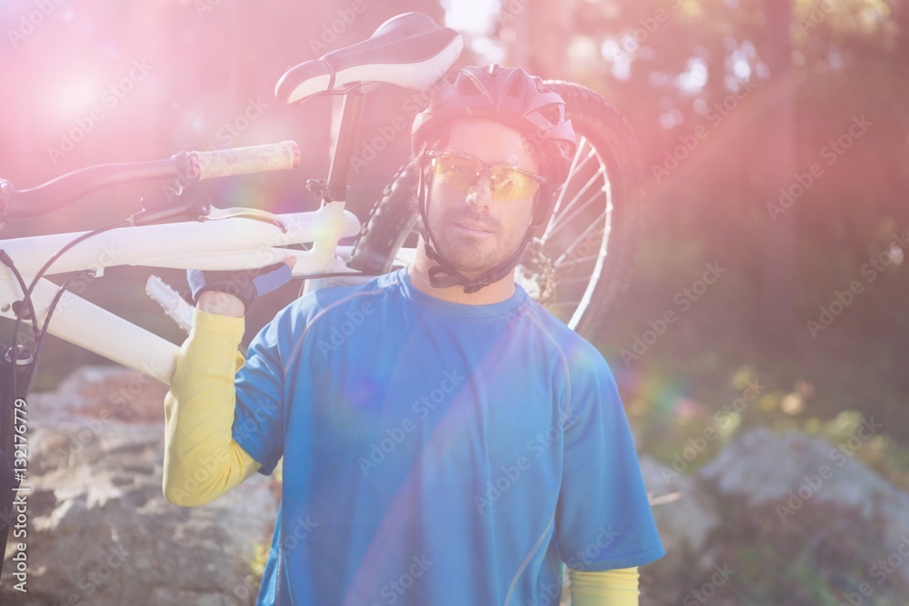 Portrait of male mountain biker carrying bicycle in forest