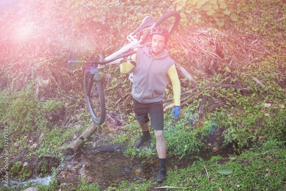 Portrait  of male mountain biker carrying bicycle in forest