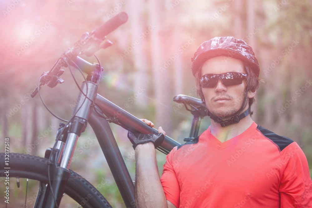 Portrait of male mountain biker carrying bicycle in forest