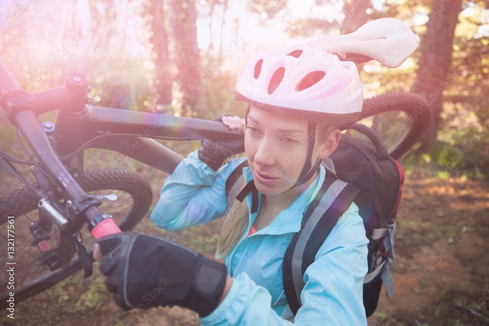 Female mountain biker carrying her bicycle in forest