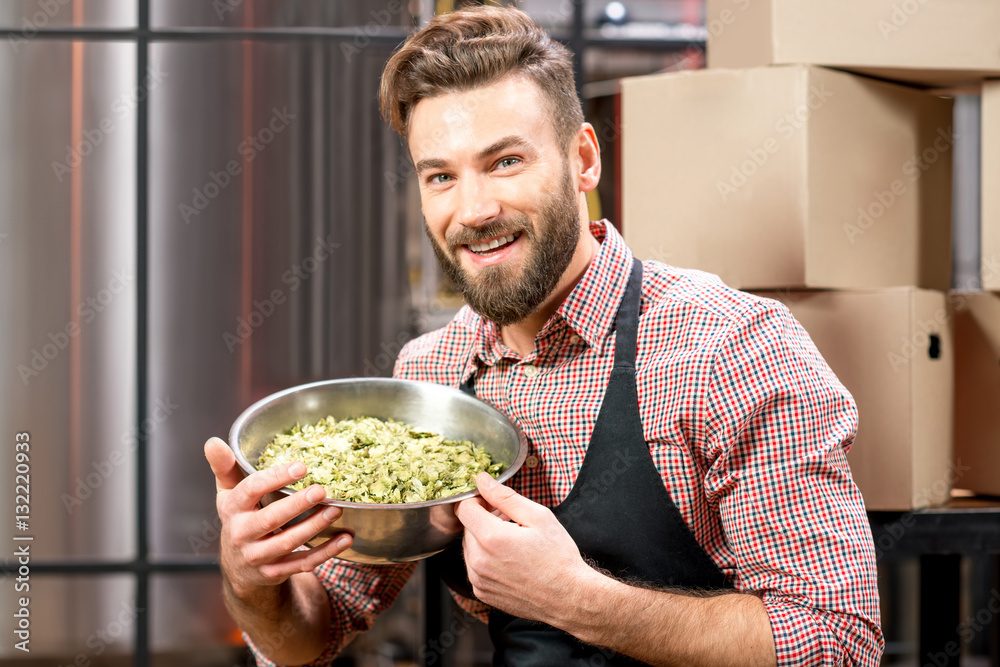 Portrait of a brewer with green hops dressed in apron and checkered shirt at the manufacturing