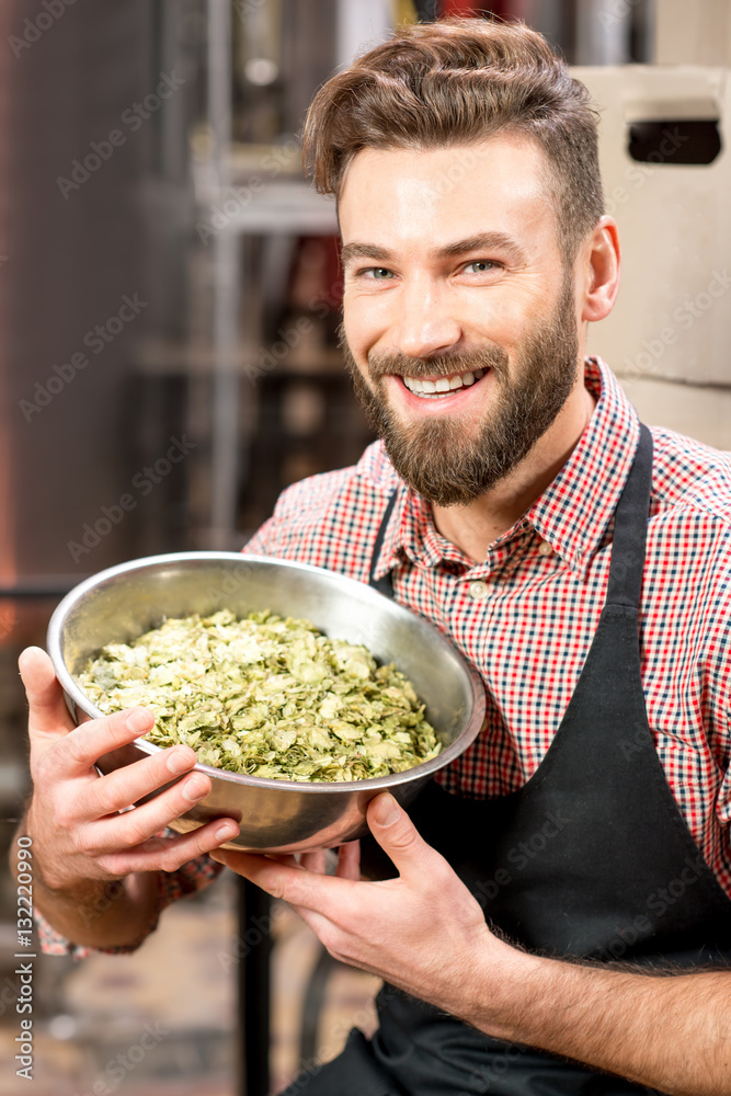 Portrait of a brewer with green hops dressed in apron and checkered shirt at the manufacturing