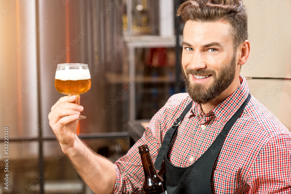 Handsome brewer expertising beer in the glass at the manufacturing