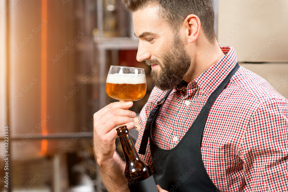 Handsome brewer expertising beer in the glass at the manufacturing