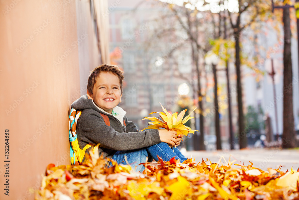 Happy boy sitting in leaf pile with rucksack