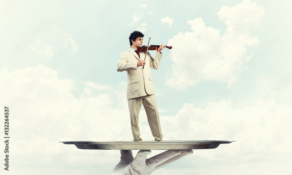 Businessman on metal tray playing violin against blue sky background