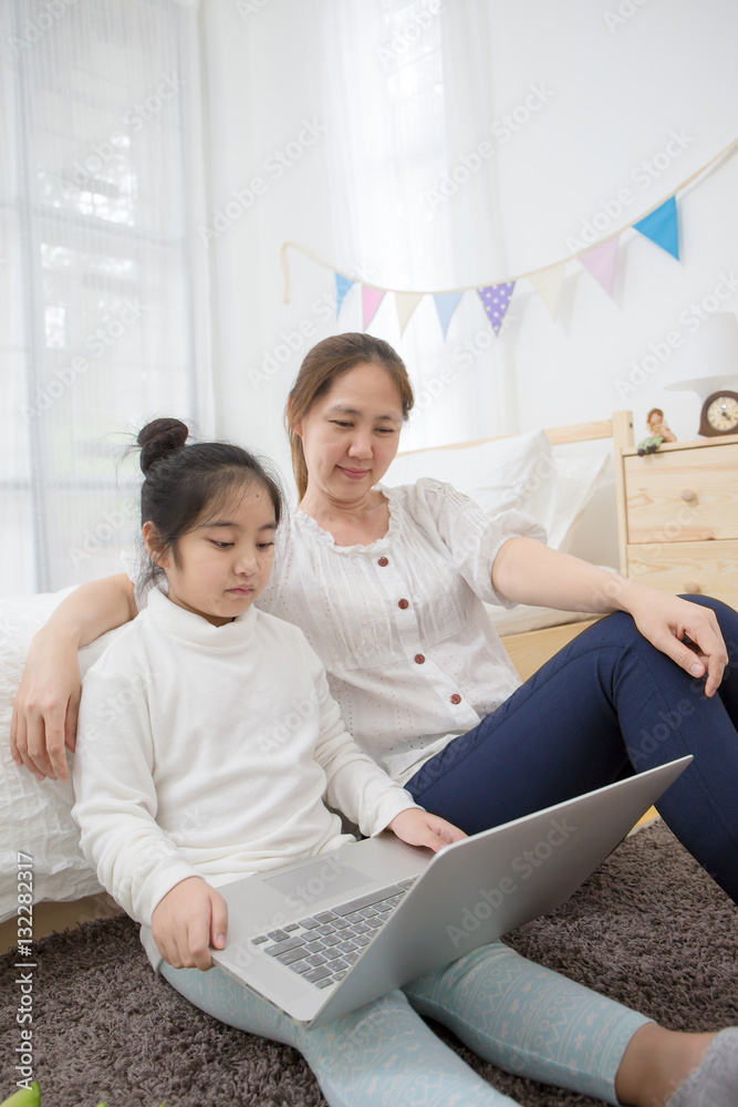 Asian mother and daughter using laptop together in bedroom