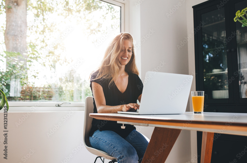 Beautiful young woman working on laptop in kitchen