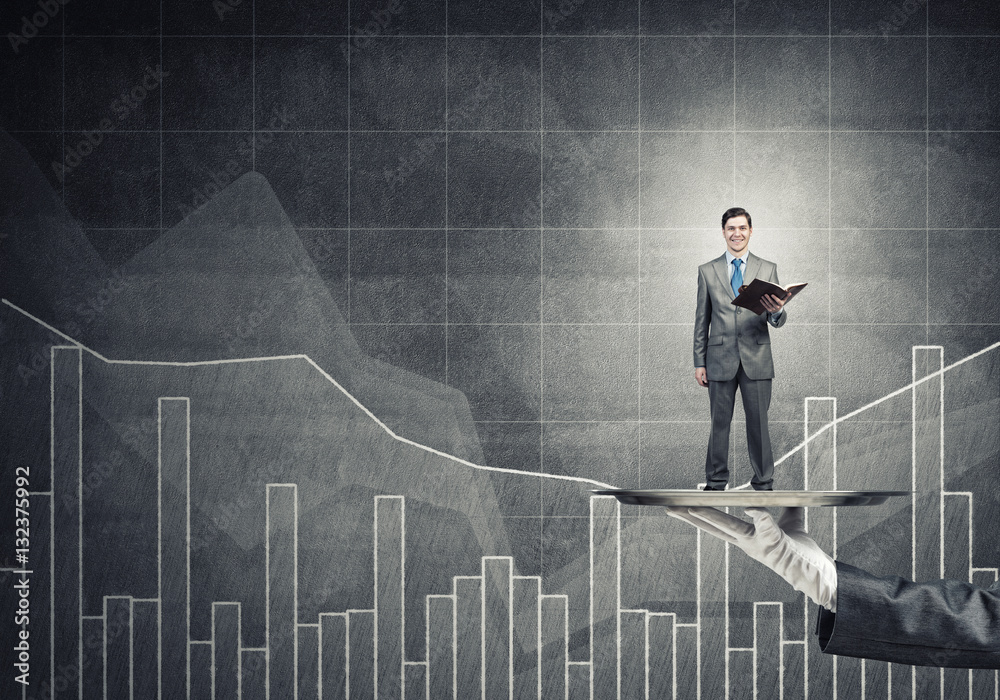 Businessman on metal tray with red book in hands against concrete background with chart