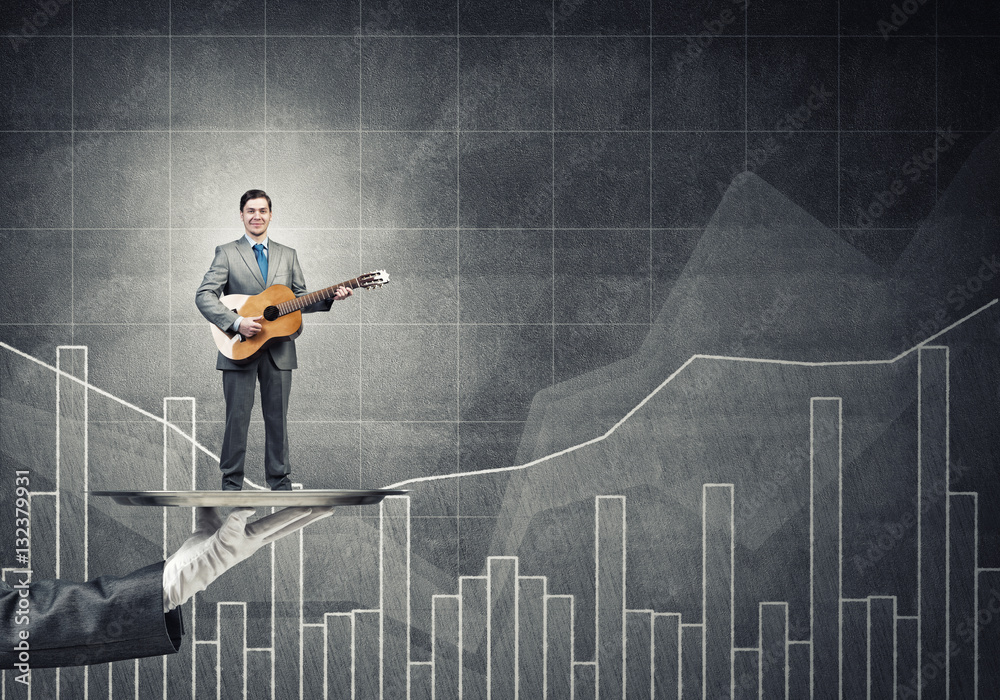 Businessman on metal tray playing acoustic guitar against graphs background