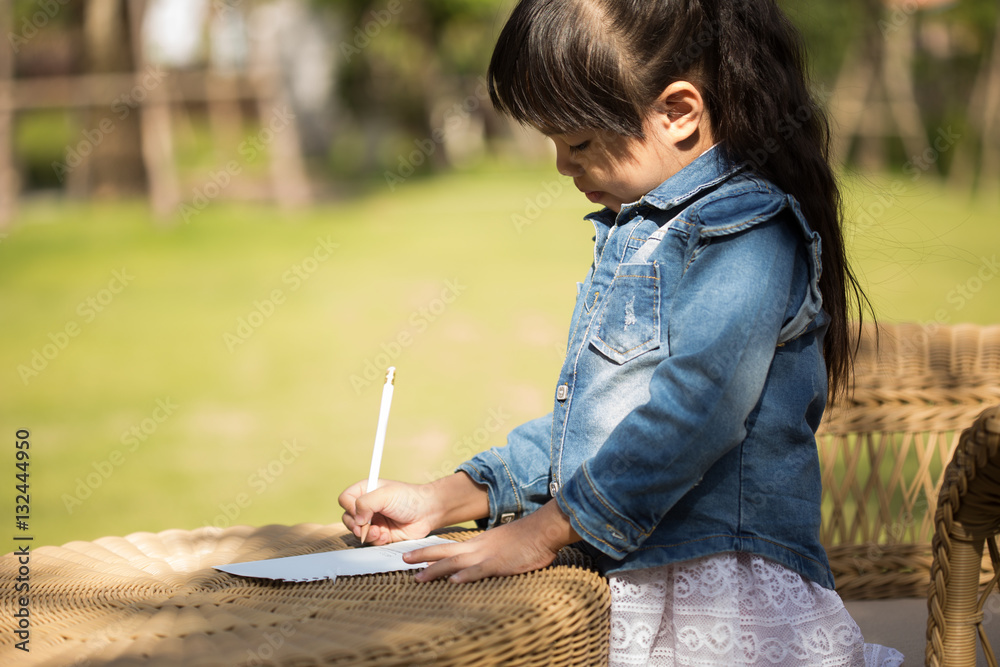 Little asian girl writing on notebook in the park