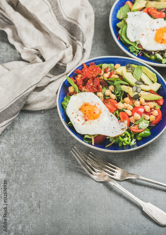 Healthy breakfast with fried egg, chickpea sprouts, seeds, fresh vegetables and greens in bowls over