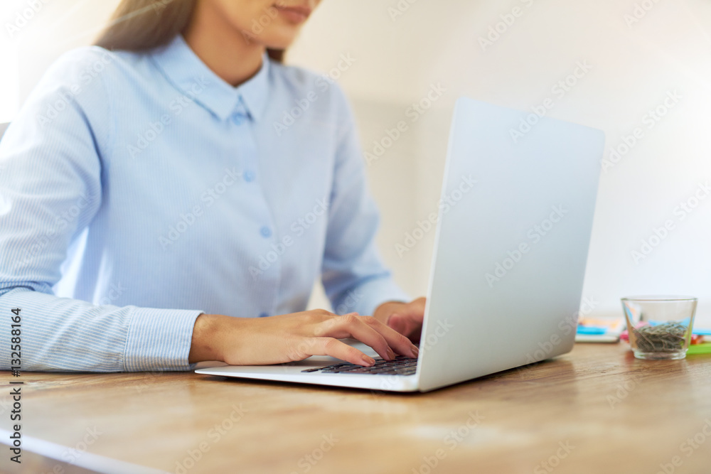 Hands of partially obscured woman typing on laptop