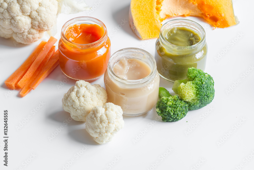 baby mashed with spoon in glass jar on white background