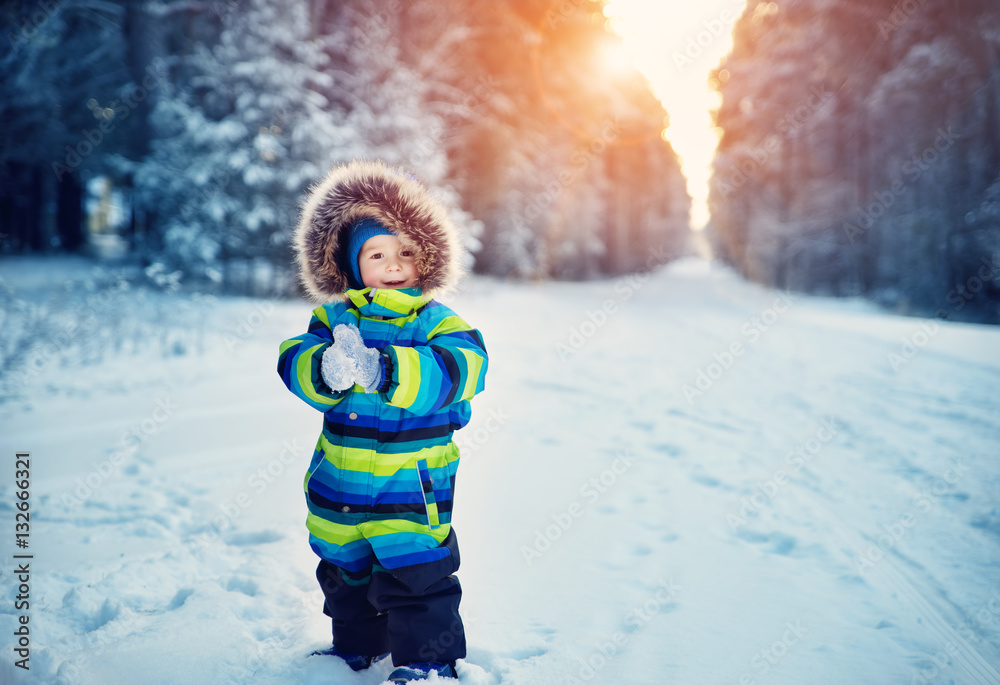 Boy in knitted hat, gloves and scarf outdoors at snowfall