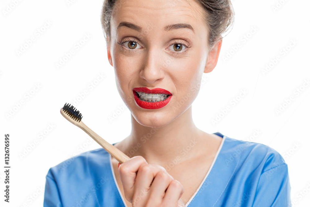 Portrait of confused woman with tooth braces holding a toothbrush on the white background. Woman wor