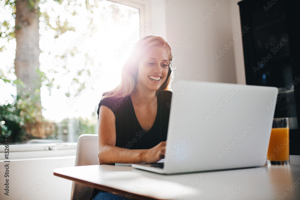 Happy female relaxing in kitchen with laptop