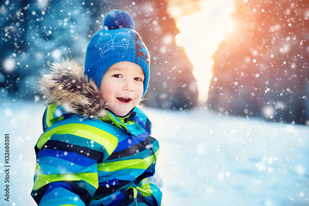 Boy in knitted hat, gloves and scarf outdoors at snowfall