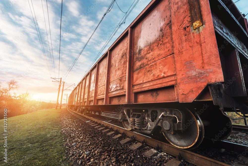 Railway station with cargo wagons and train against sunny sky with clouds in the evening. Colorful i