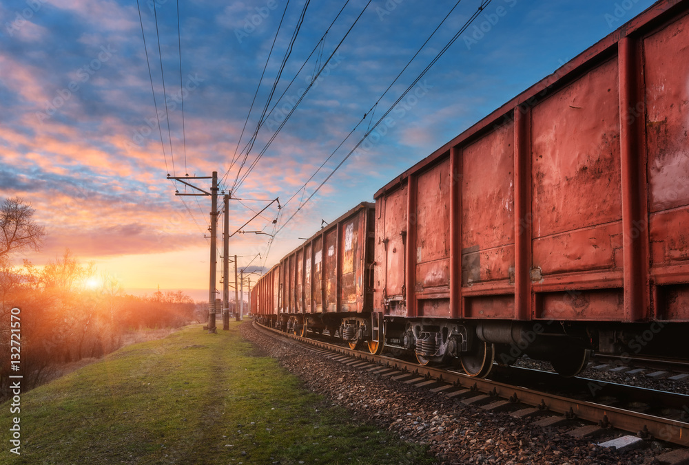 Railway station with cargo wagons and train against sunny sky with clouds in the evening. Colorful i