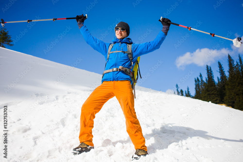 Man with trekking poles goes through the snow in the mountains.