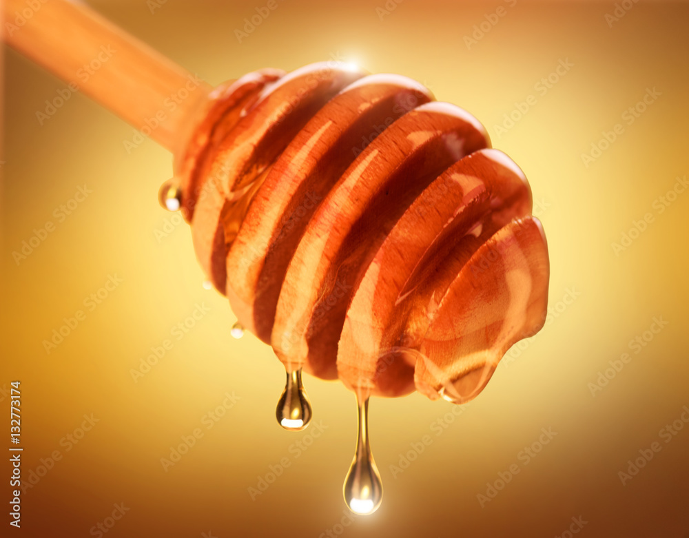 Honey dripping from honey dipper isolated on yellow. Thick honey dipping from the wooden honey spoon