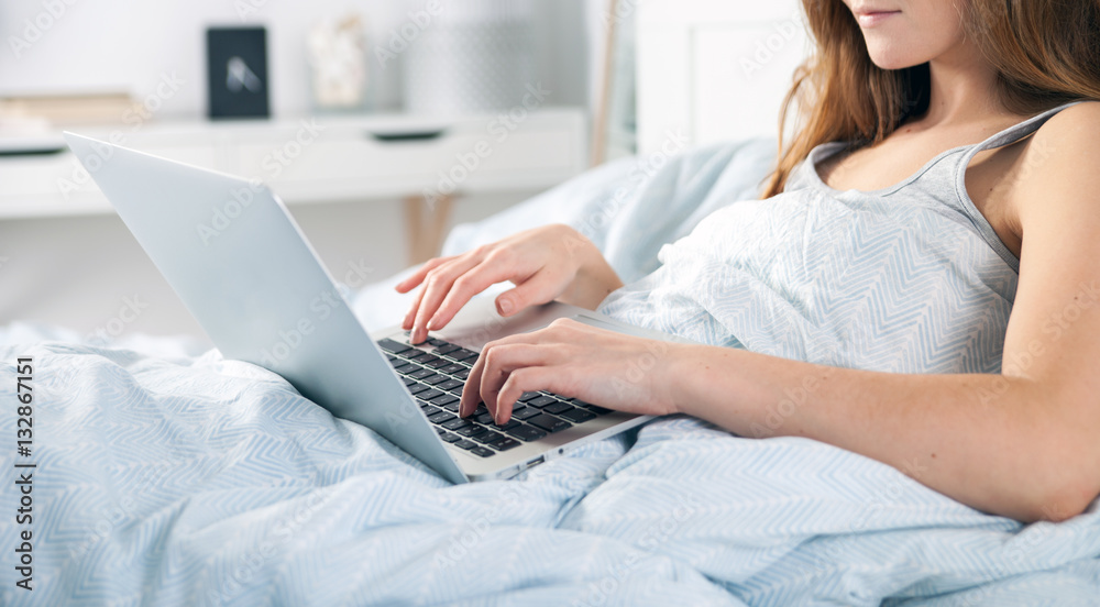 Young girl with laptop checking social media in bed at home